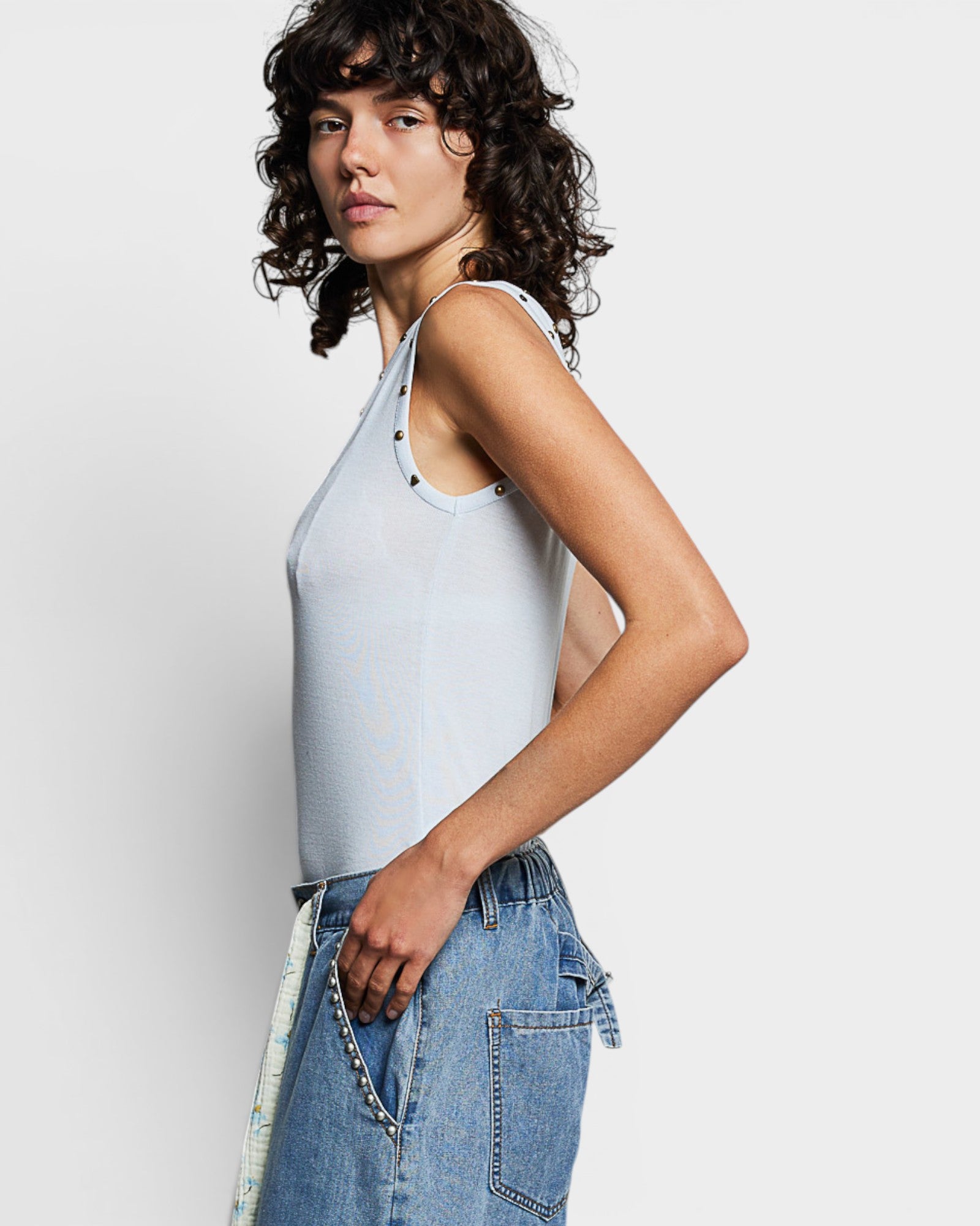 Woman wearing a light blue tank top and denim jeans against a plain background