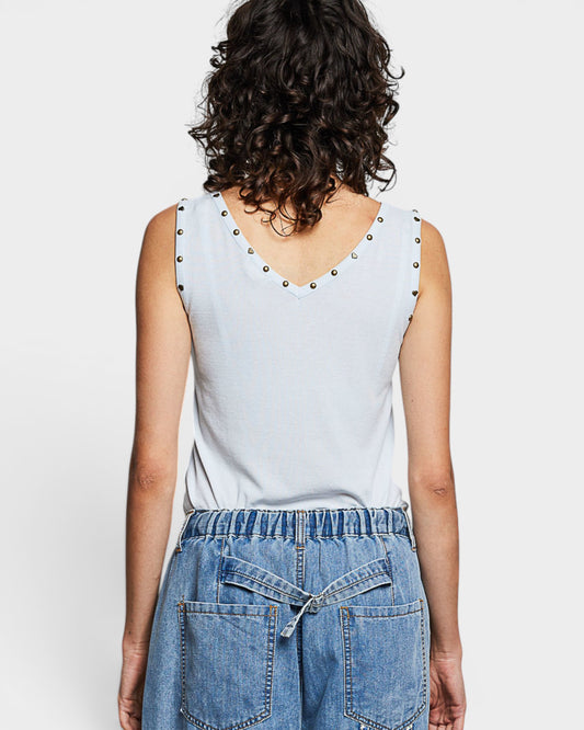 Person wearing a light blue sleeveless top with studded details and blue jeans on a white background