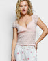Woman wearing a pink lace top and white pants with floral patterns on a light background