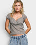 Woman wearing a patterned gray top and denim shorts against a plain background