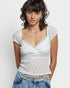 Woman wearing a white lace top and blue jeans against a plain background