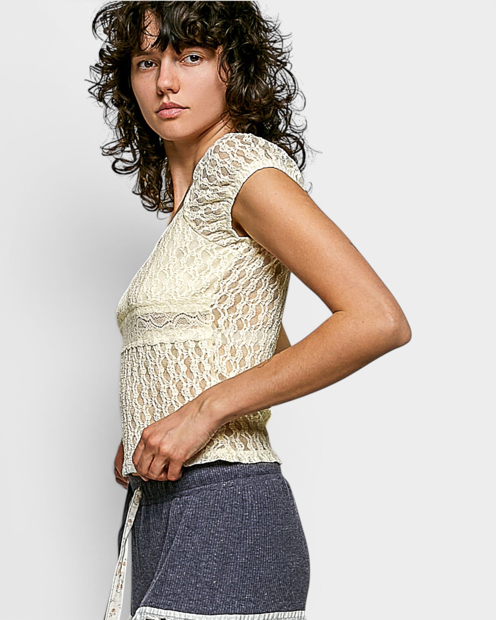 Woman wearing a lace top and dark pants against a light background