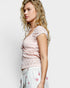 Woman wearing a pink lace top and white pants with floral embroidery on a light gray background