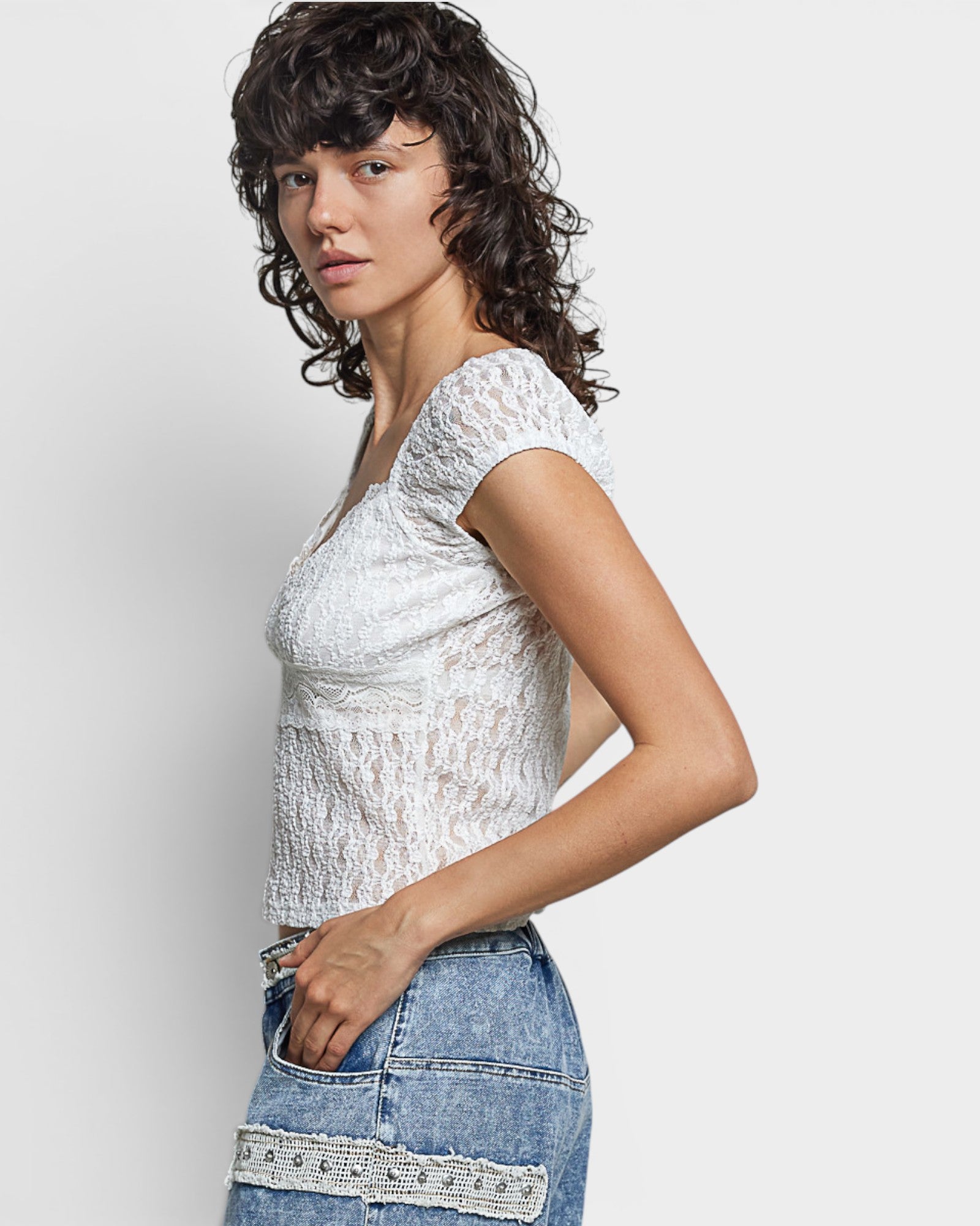 Woman wearing a white lace top and blue denim skirt on a light gray background