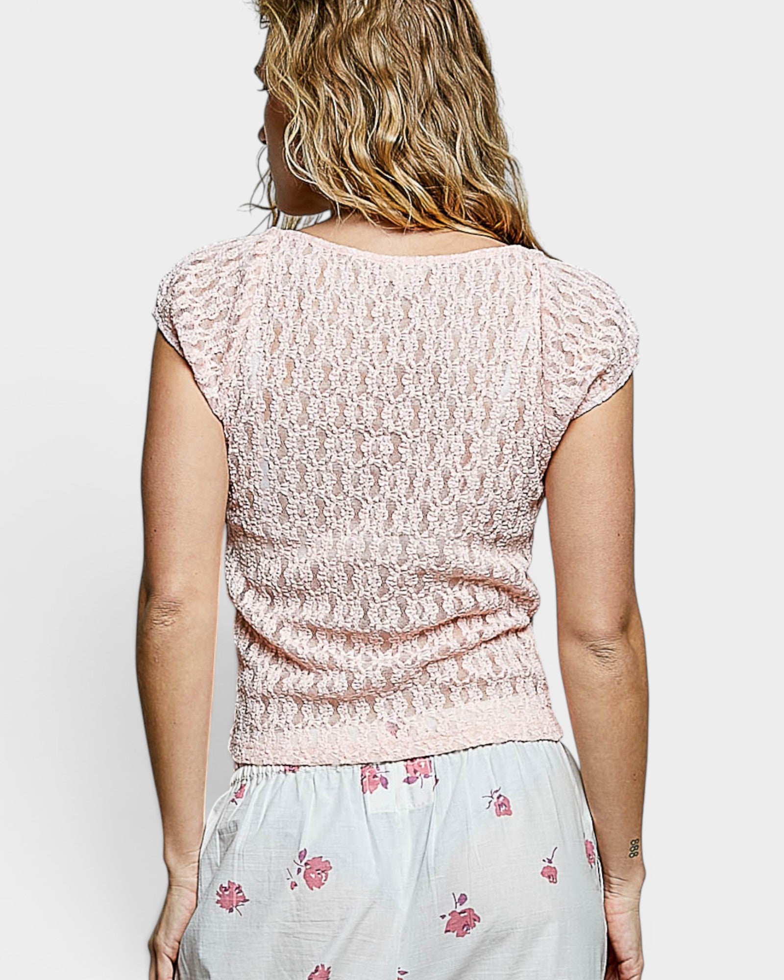 Woman wearing a light pink lace top and floral skirt on a white background