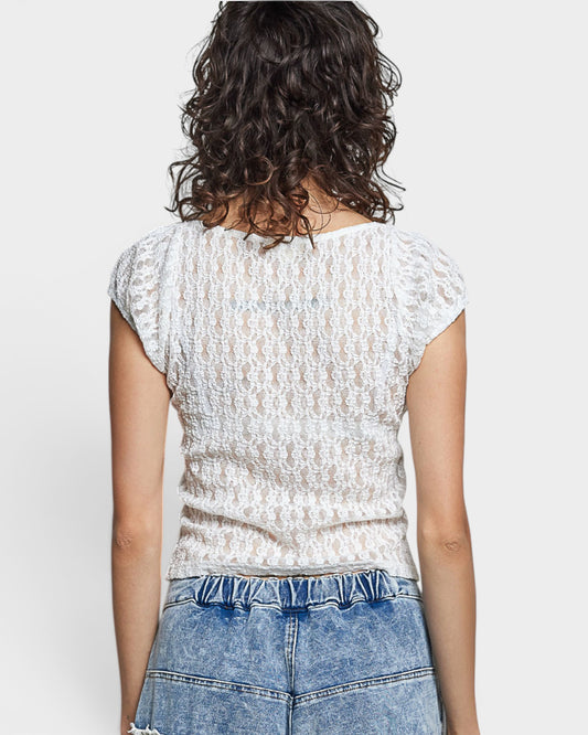 Person wearing a white textured top and blue jeans on a plain background