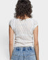 Person wearing a white textured top and blue jeans on a plain background