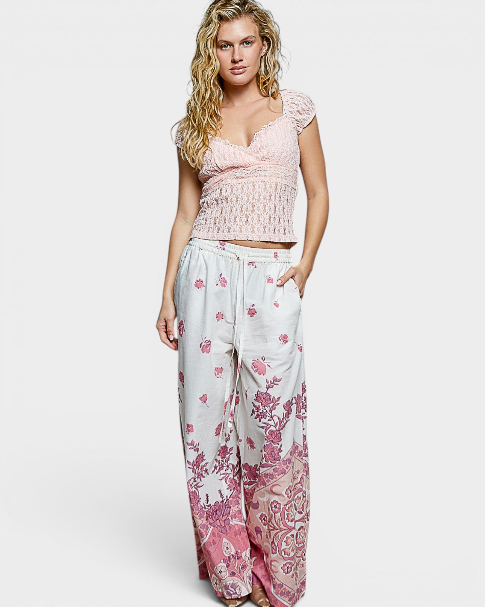 Woman wearing a pink lace top and floral pants on a white background