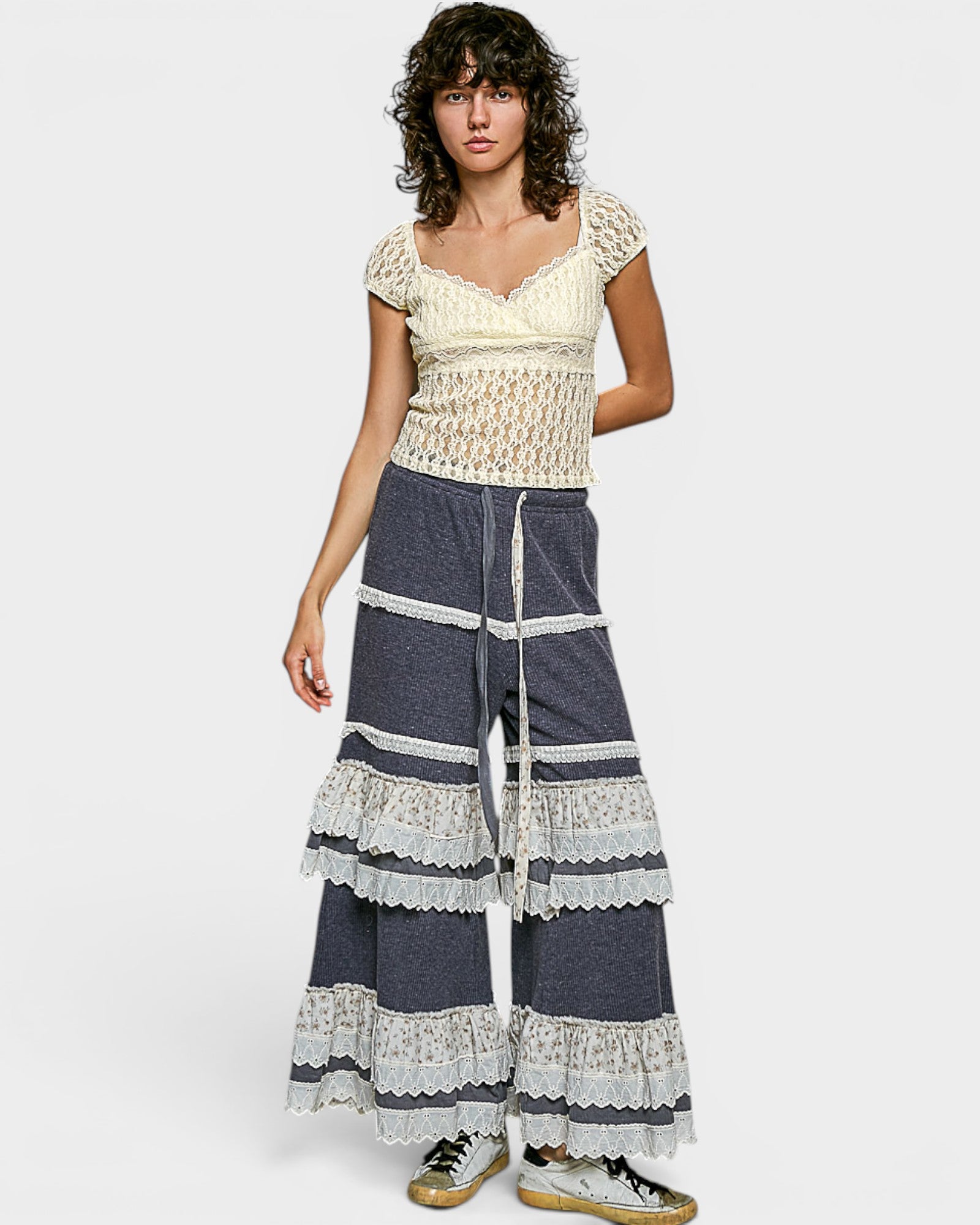 Woman wearing a white lace top and blue striped pants on a white background