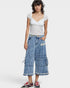 Woman wearing a white lace top and blue denim culottes on a plain background