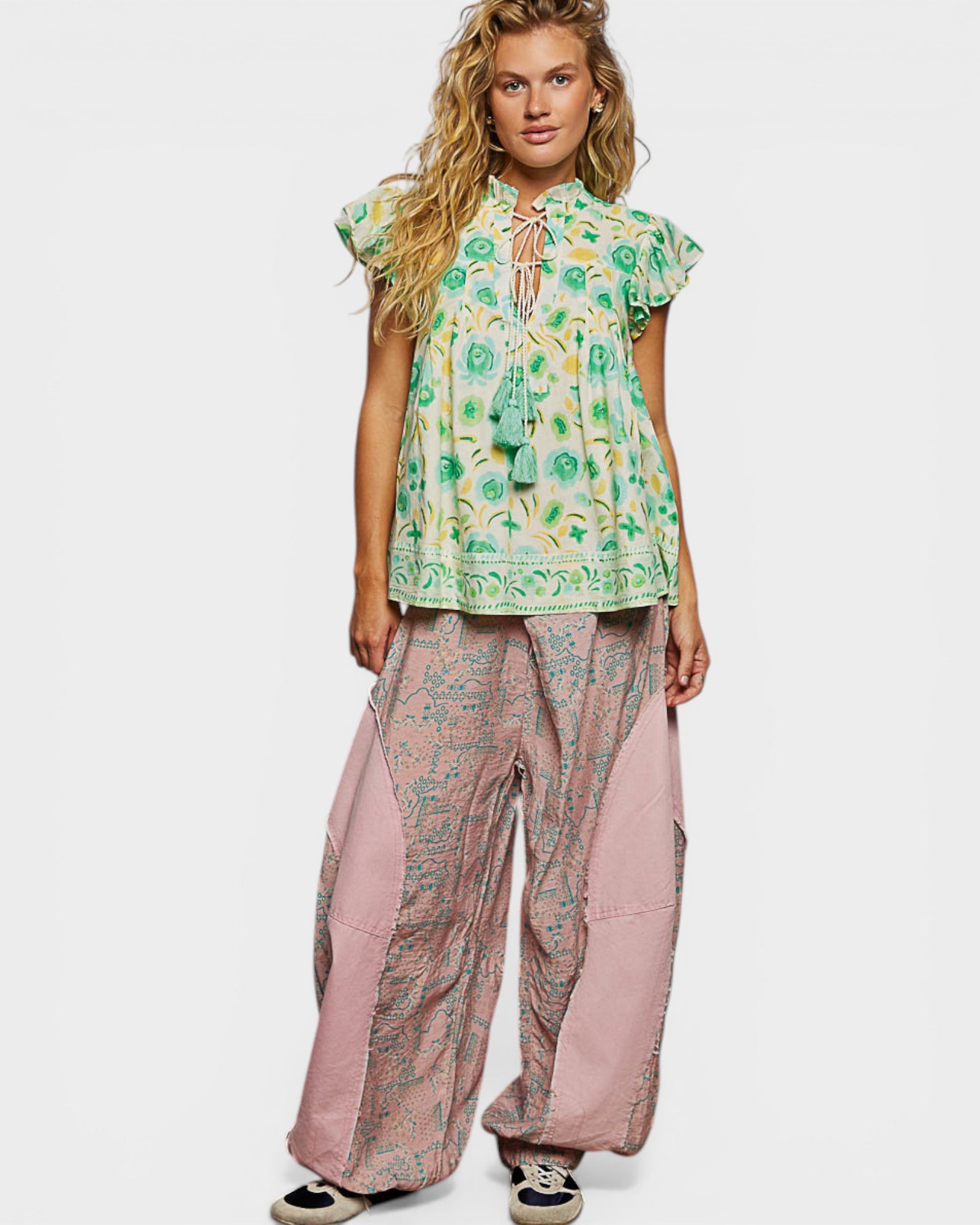 Woman wearing a green floral top and pink patterned pants on a white background