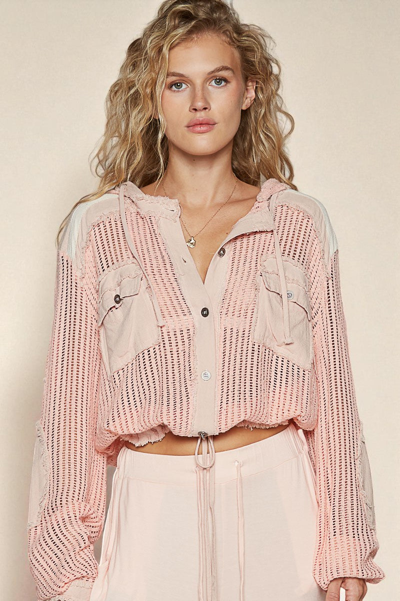 Woman wearing a pink knit cardigan over a sheer top with a beige background