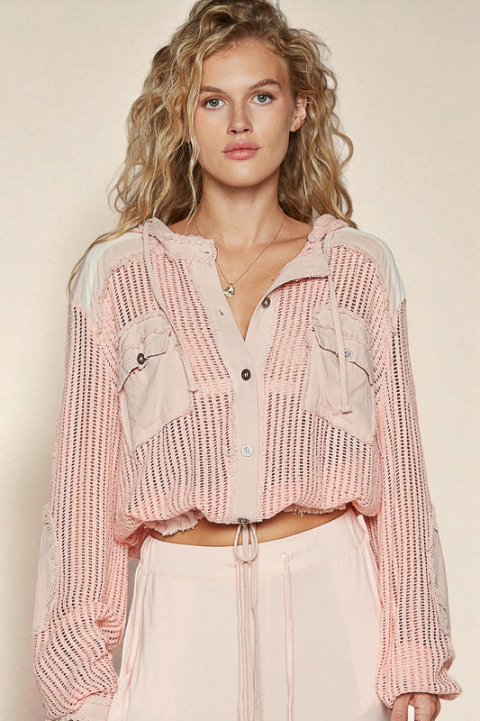 Woman wearing a pink knit cardigan over a sheer top with a beige background