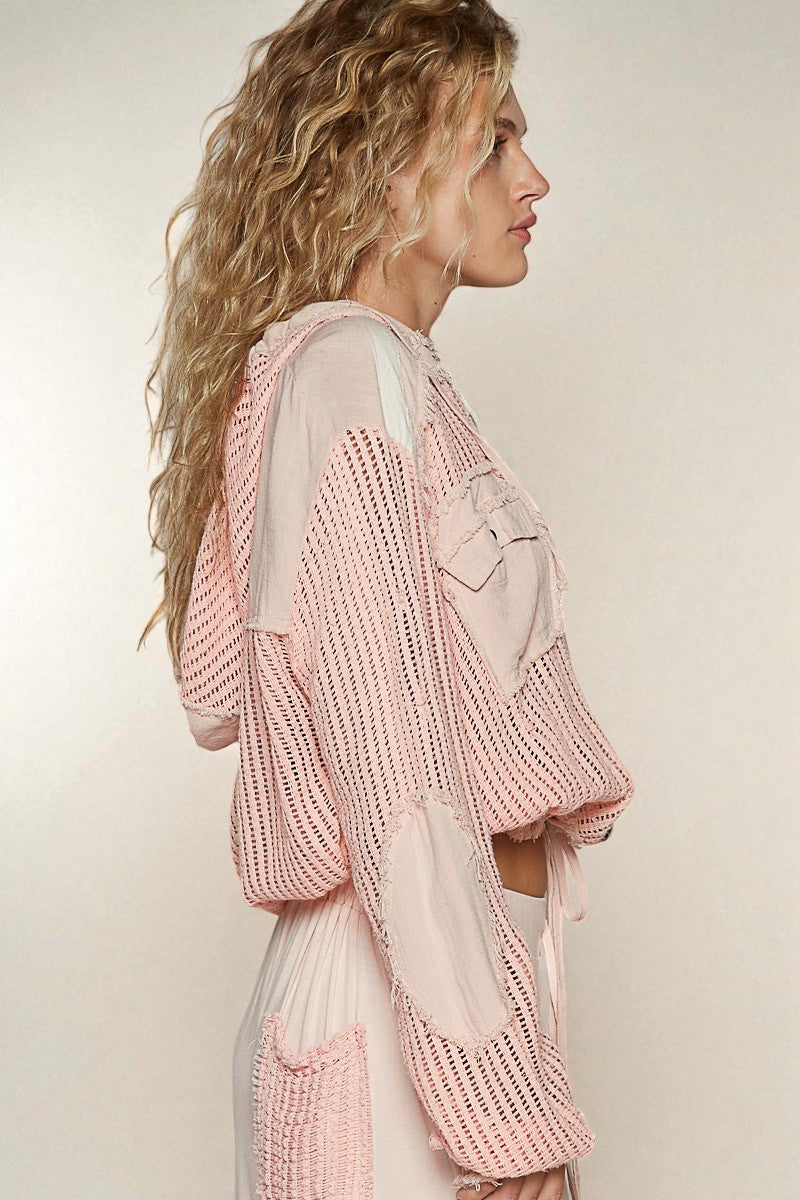 Woman wearing a pink knitted cardigan over a sheer top against a plain background