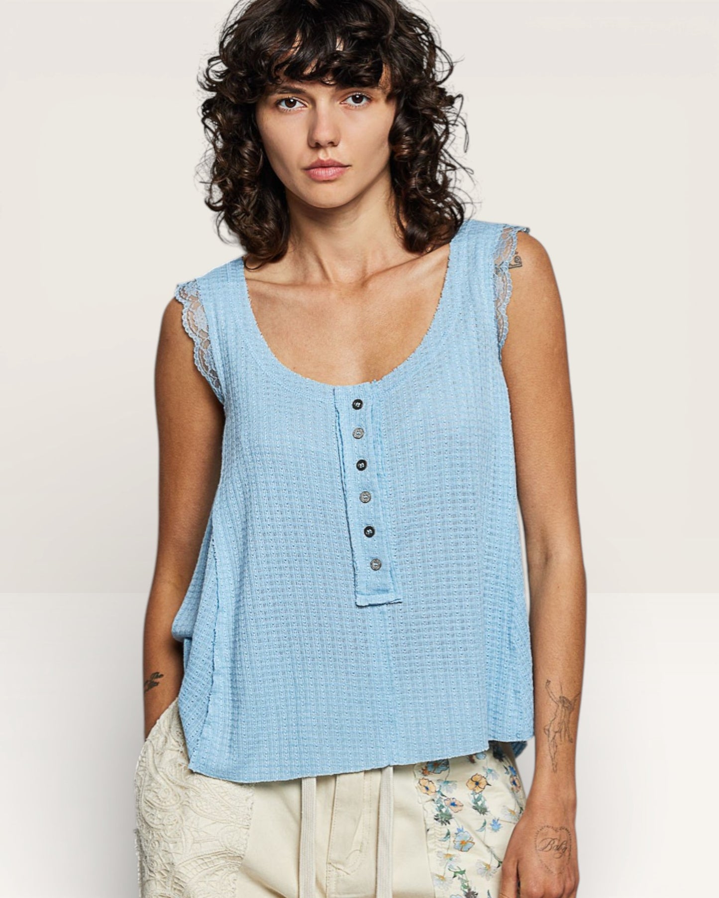 Woman wearing a light blue sleeveless top with buttons against a plain background