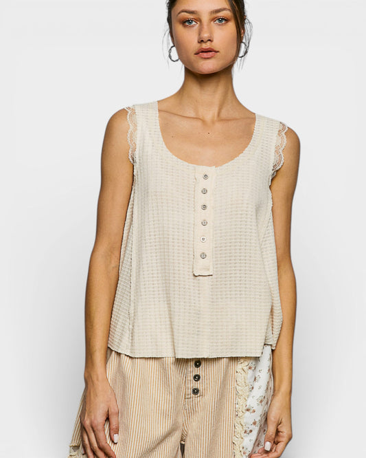 Woman wearing a beige sleeveless top with lace details on a white background
