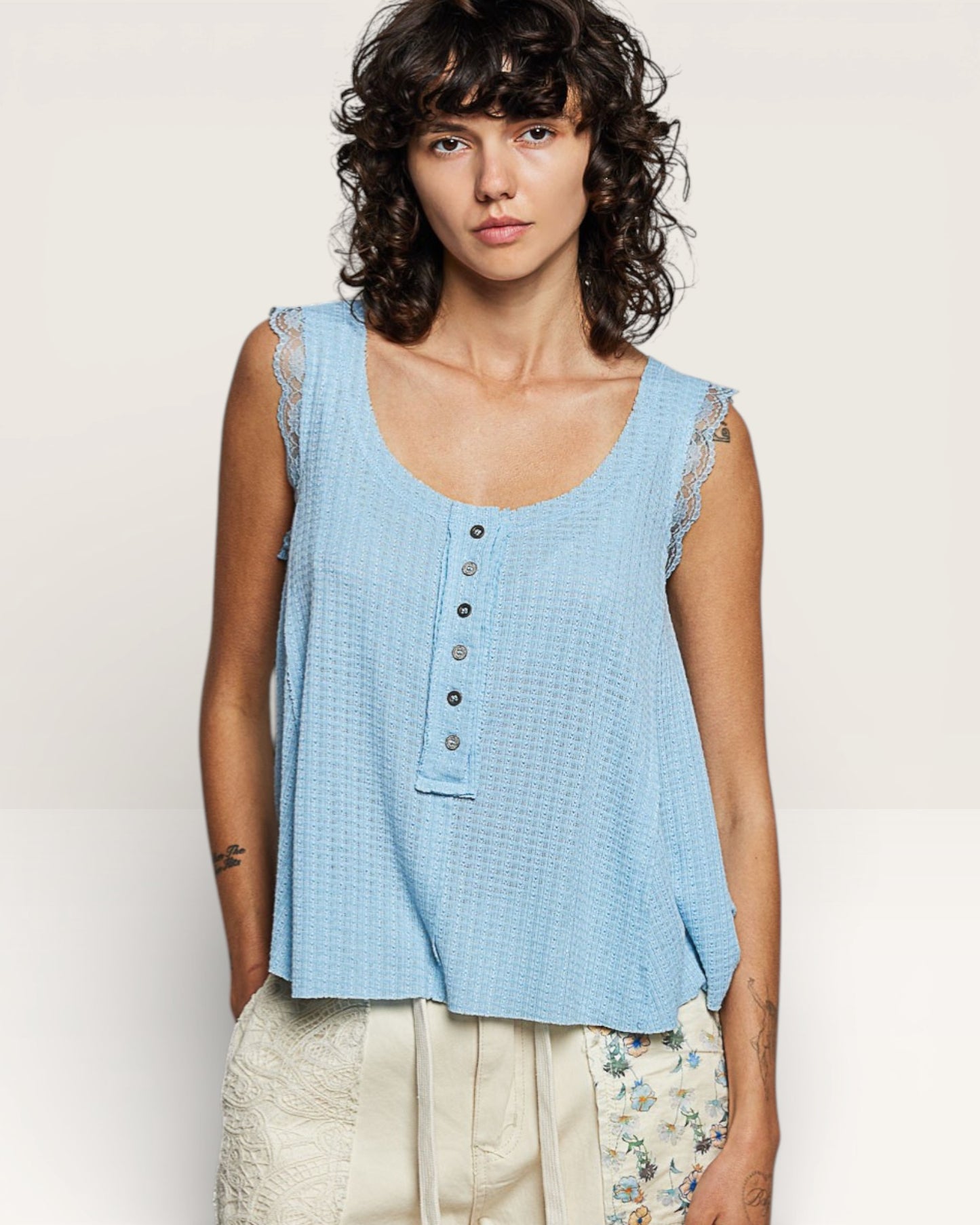 Woman wearing a light blue sleeveless top with lace details on a plain background