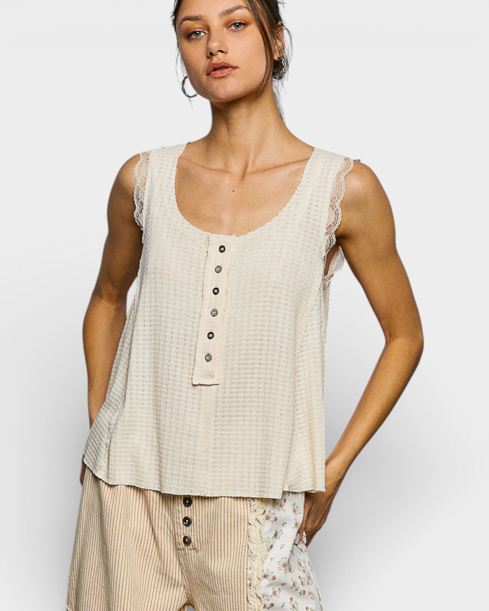 Woman wearing a beige sleeveless top with lace details on a white background
