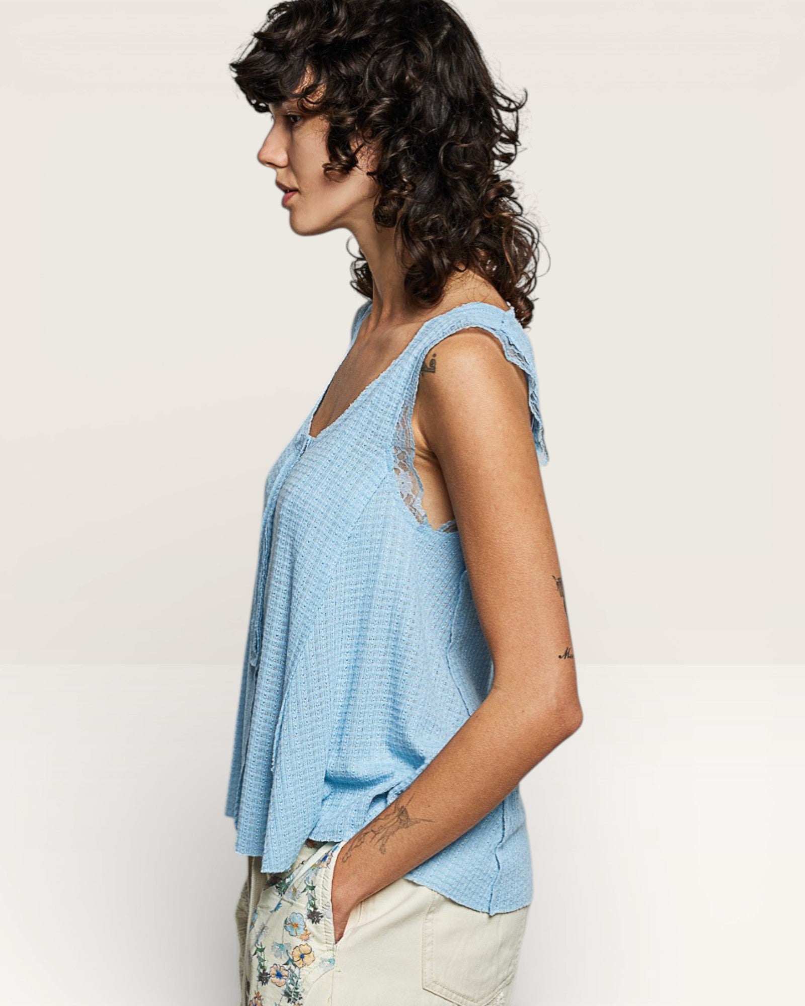 Woman wearing a light blue sleeveless top with floral pants on a plain background