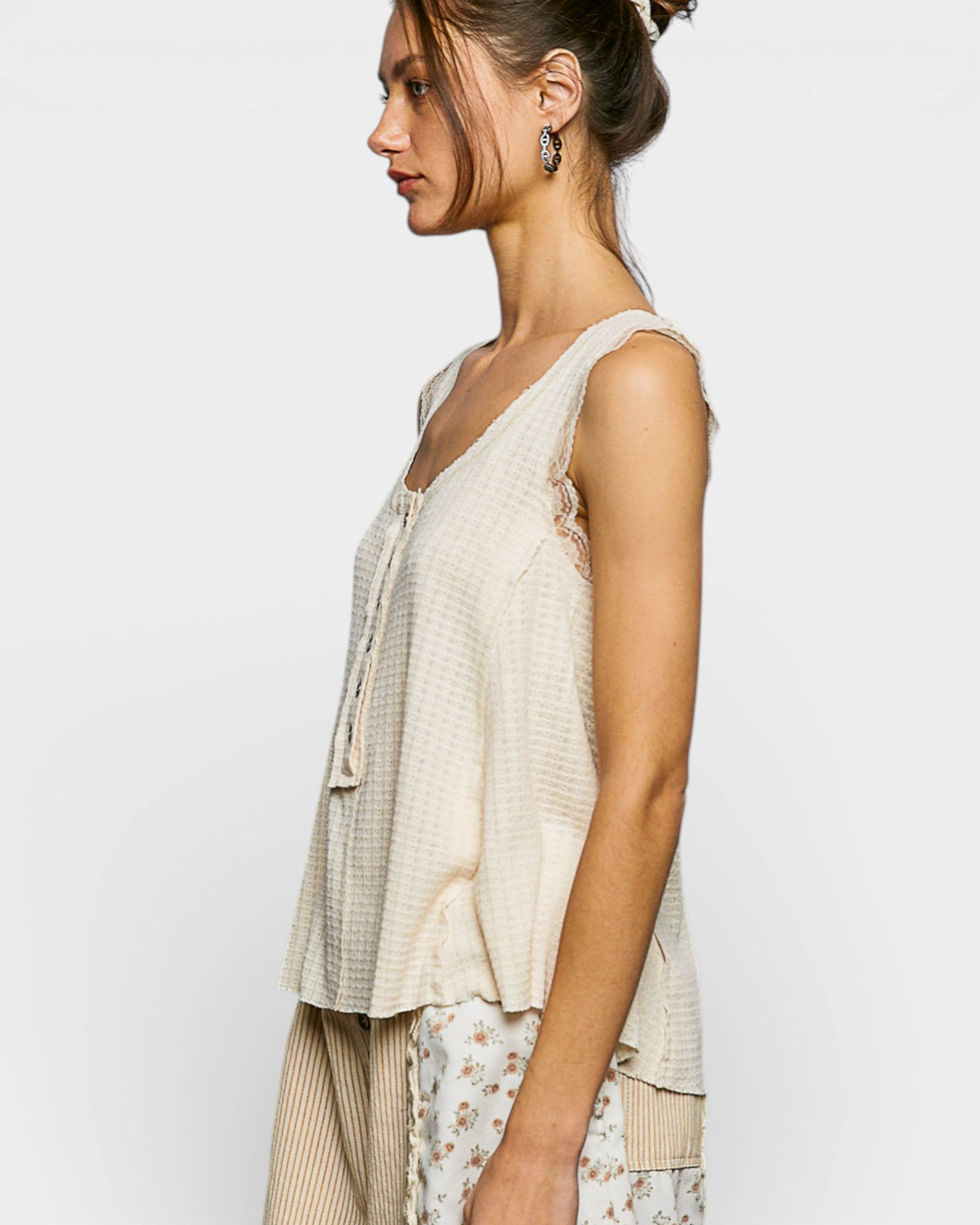 Woman wearing a beige sleeveless top with floral pants on a plain background