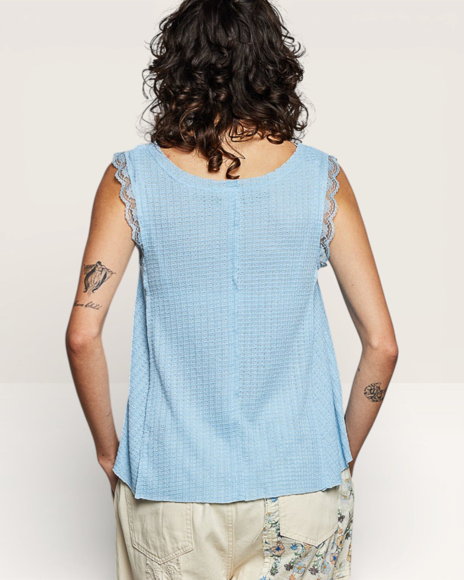 Person wearing a light blue sleeveless top with lace trim on a plain background
