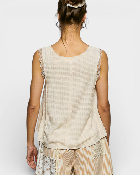 Woman wearing a beige sleeveless top with lace details on a white background