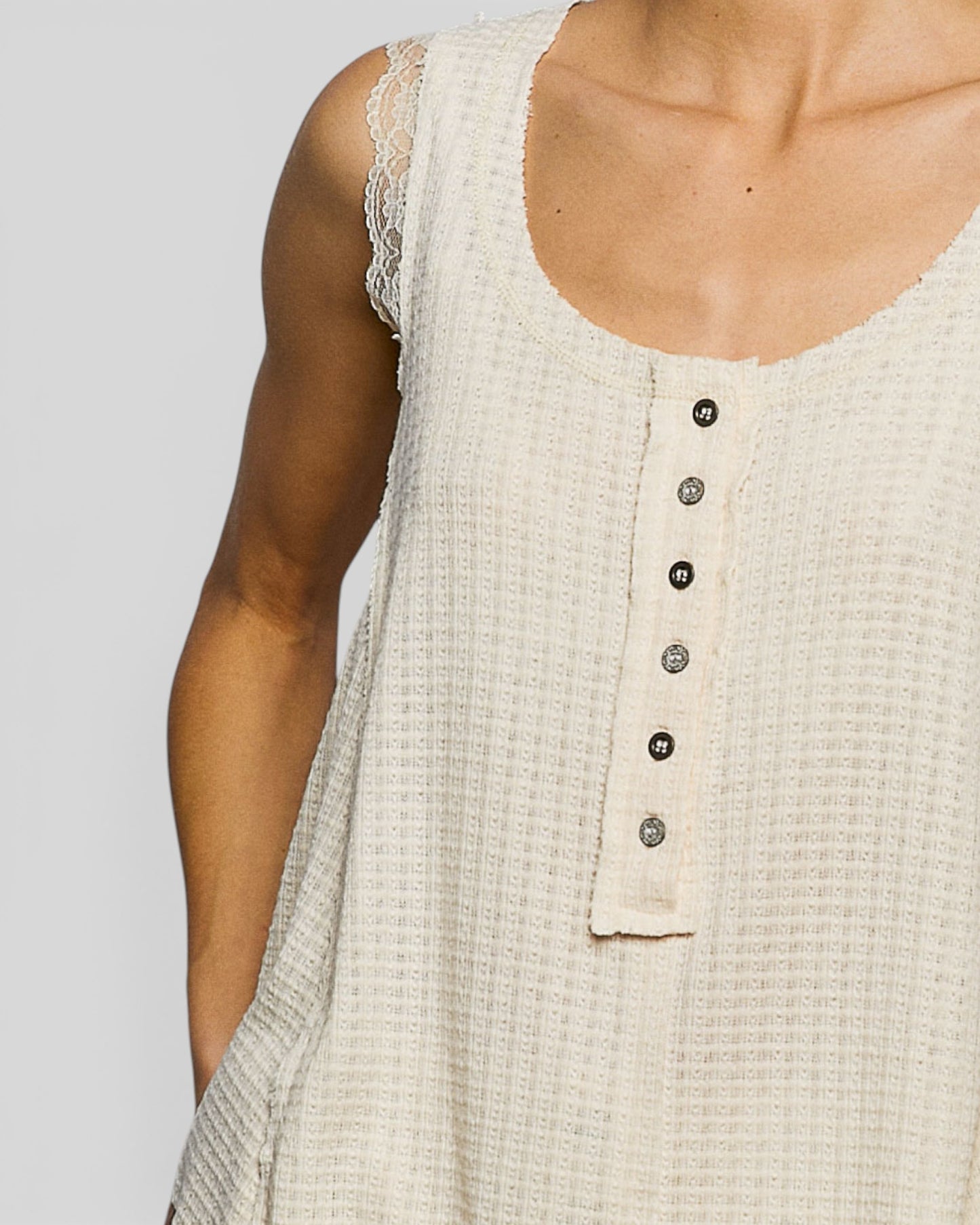 Close-up of a beige sleeveless top with buttons on a plain background