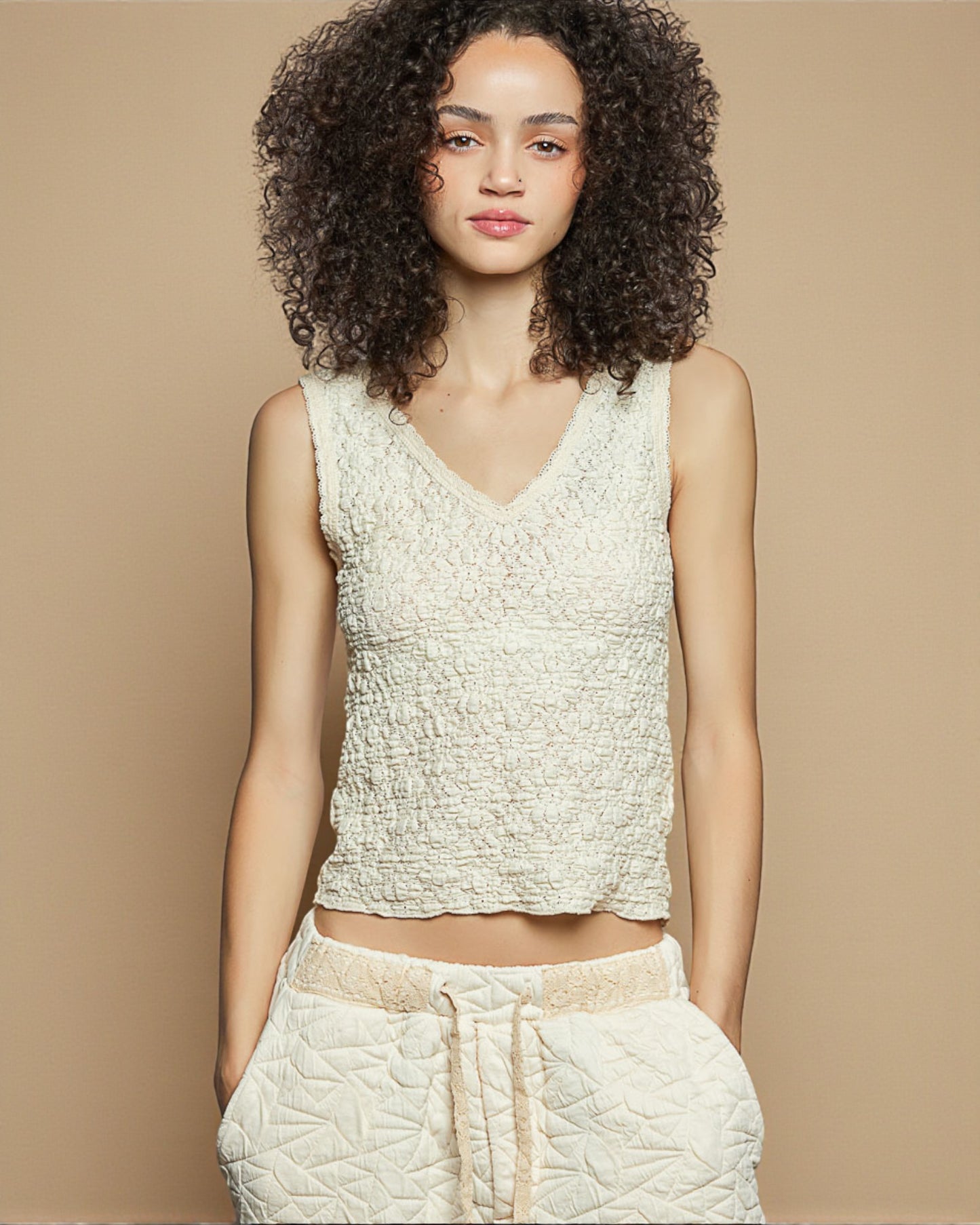 Woman wearing a textured sleeveless top and pants against a beige background
