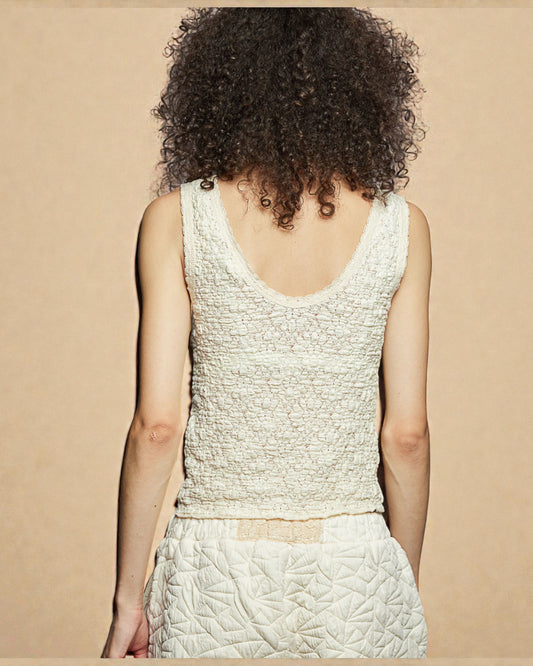 Person wearing a textured white sleeveless top and skirt set on a beige background