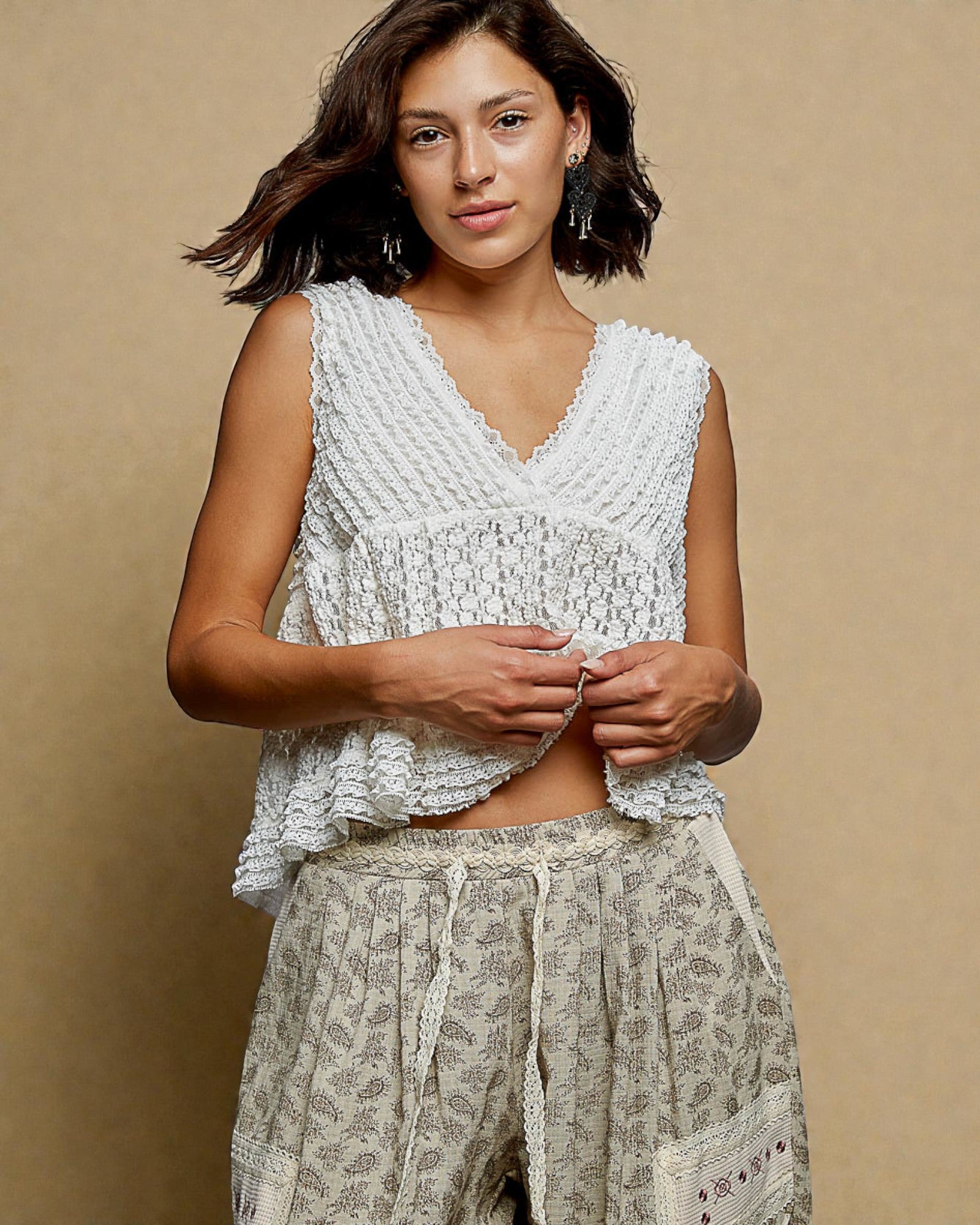 Woman wearing a white textured top and patterned pants against a beige background
