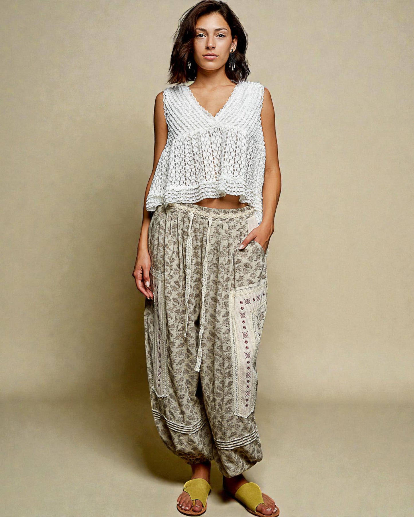 Woman wearing a white top and patterned pants against a beige background