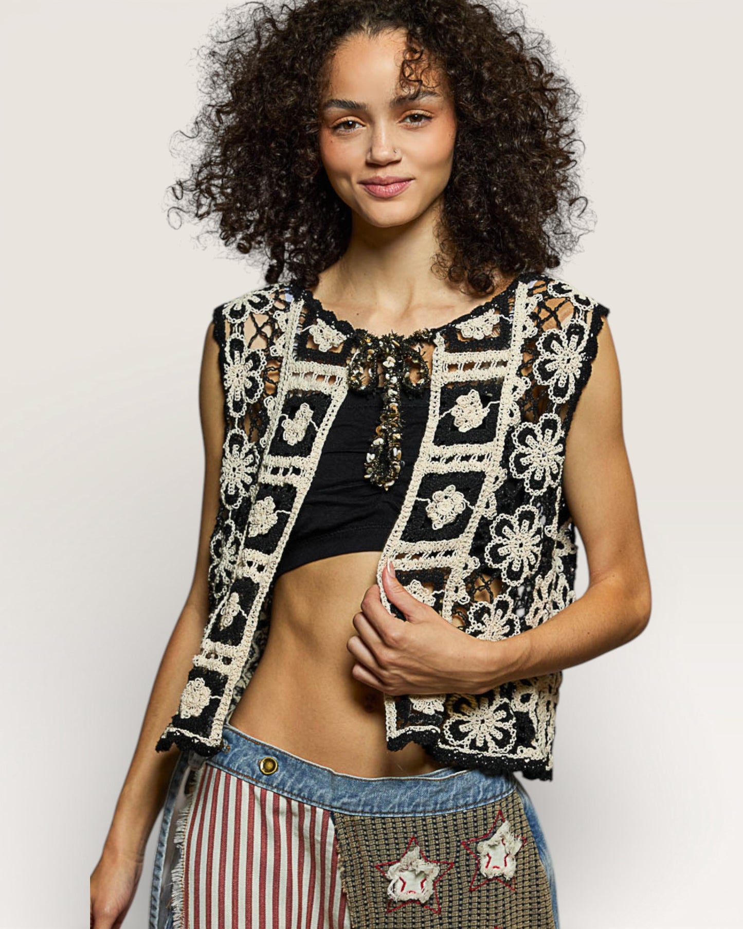 Woman wearing a black and white patterned vest over a black top with striped pants on a light gray background