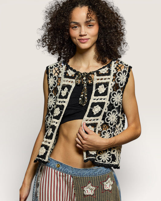 Woman wearing a black and white patterned vest over a black top with striped pants on a light gray background