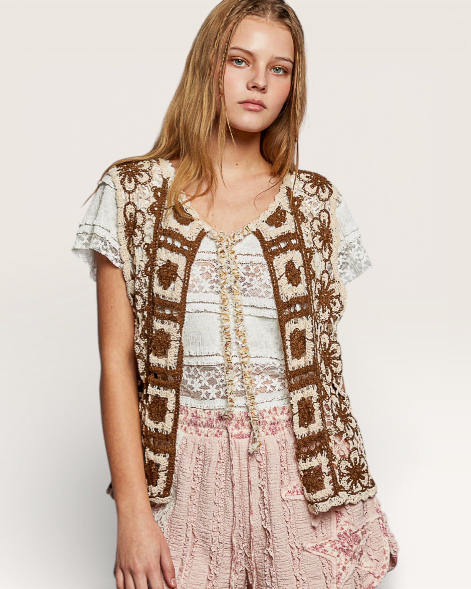 Woman wearing a patterned cardigan over a lace top and floral skirt on a plain background