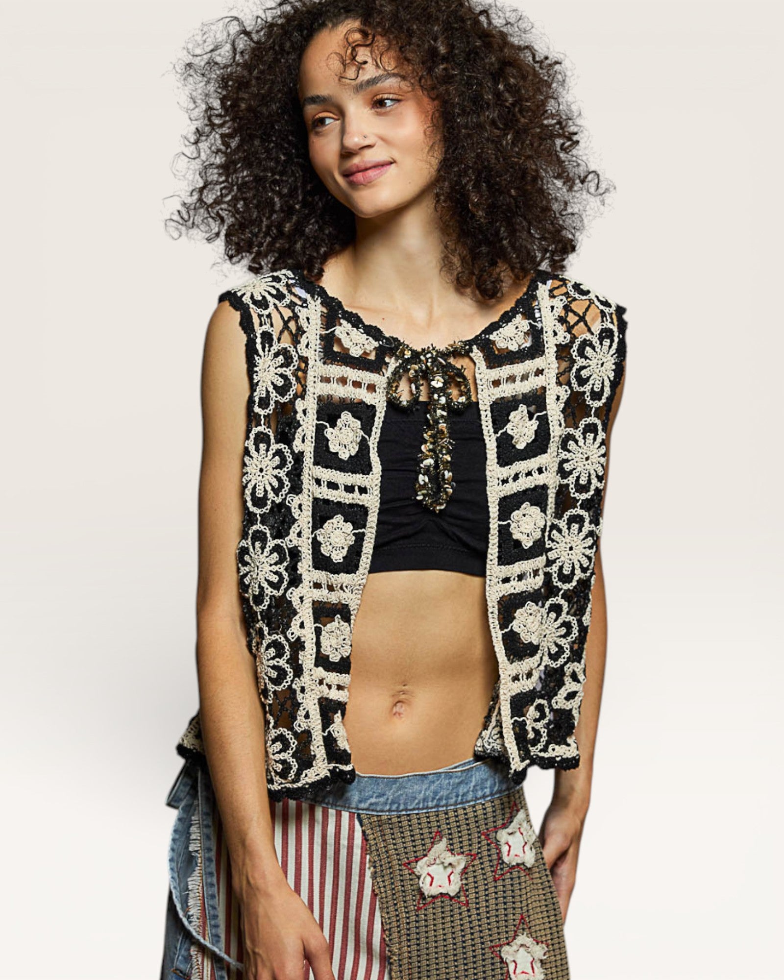 Woman wearing a black and white patterned vest over a black top with a plain background