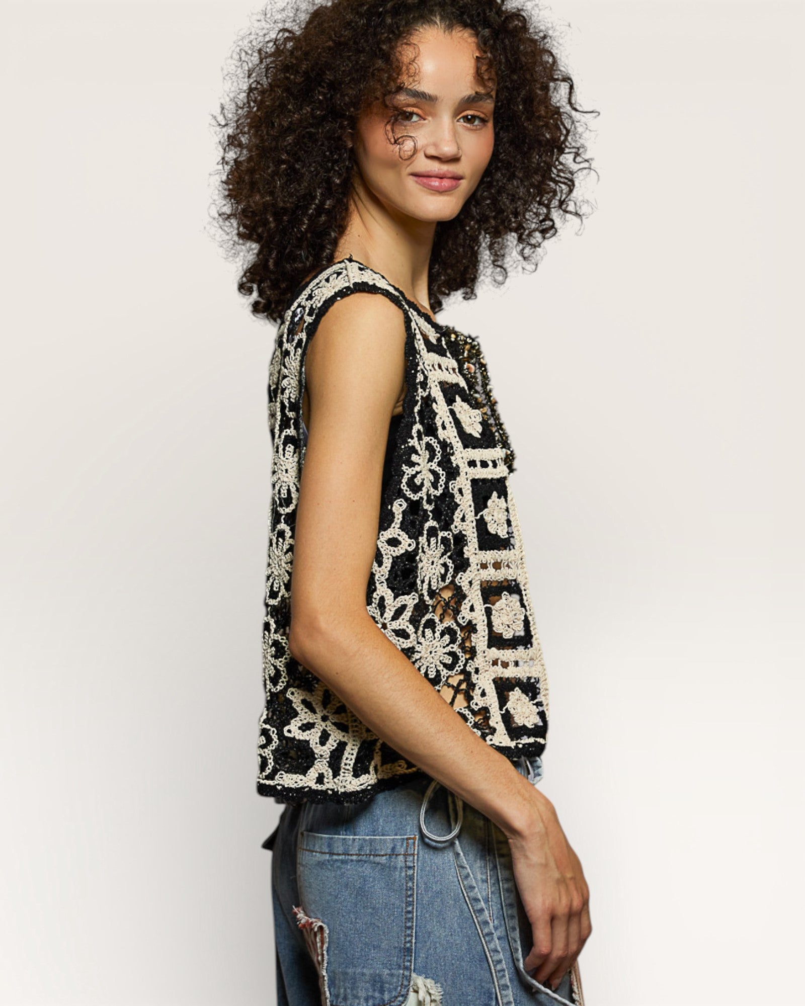 Woman wearing a black and white patterned sleeveless top with blue jeans on a light gray background