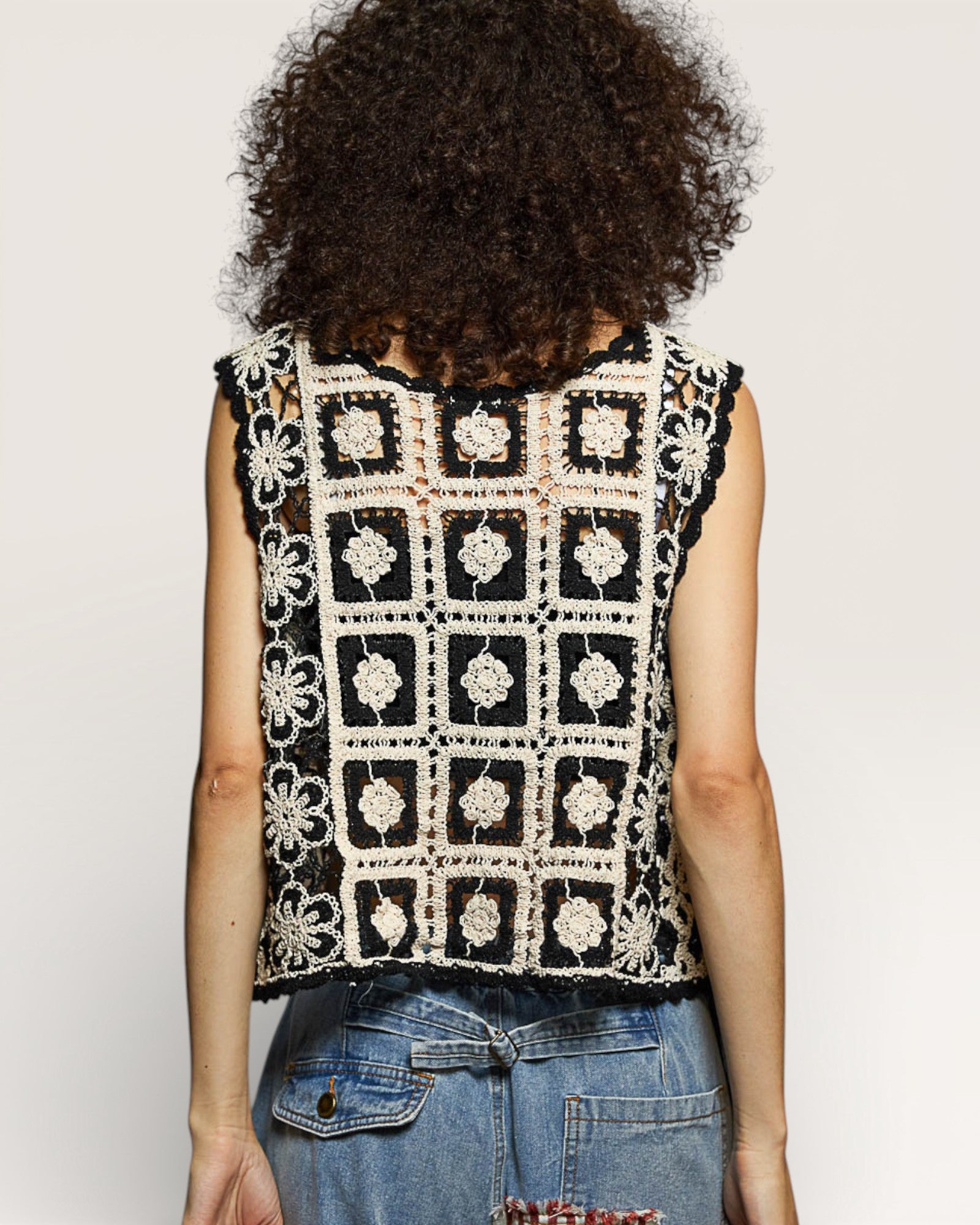 Person wearing a black and white patterned sleeveless top with denim shorts on a plain background