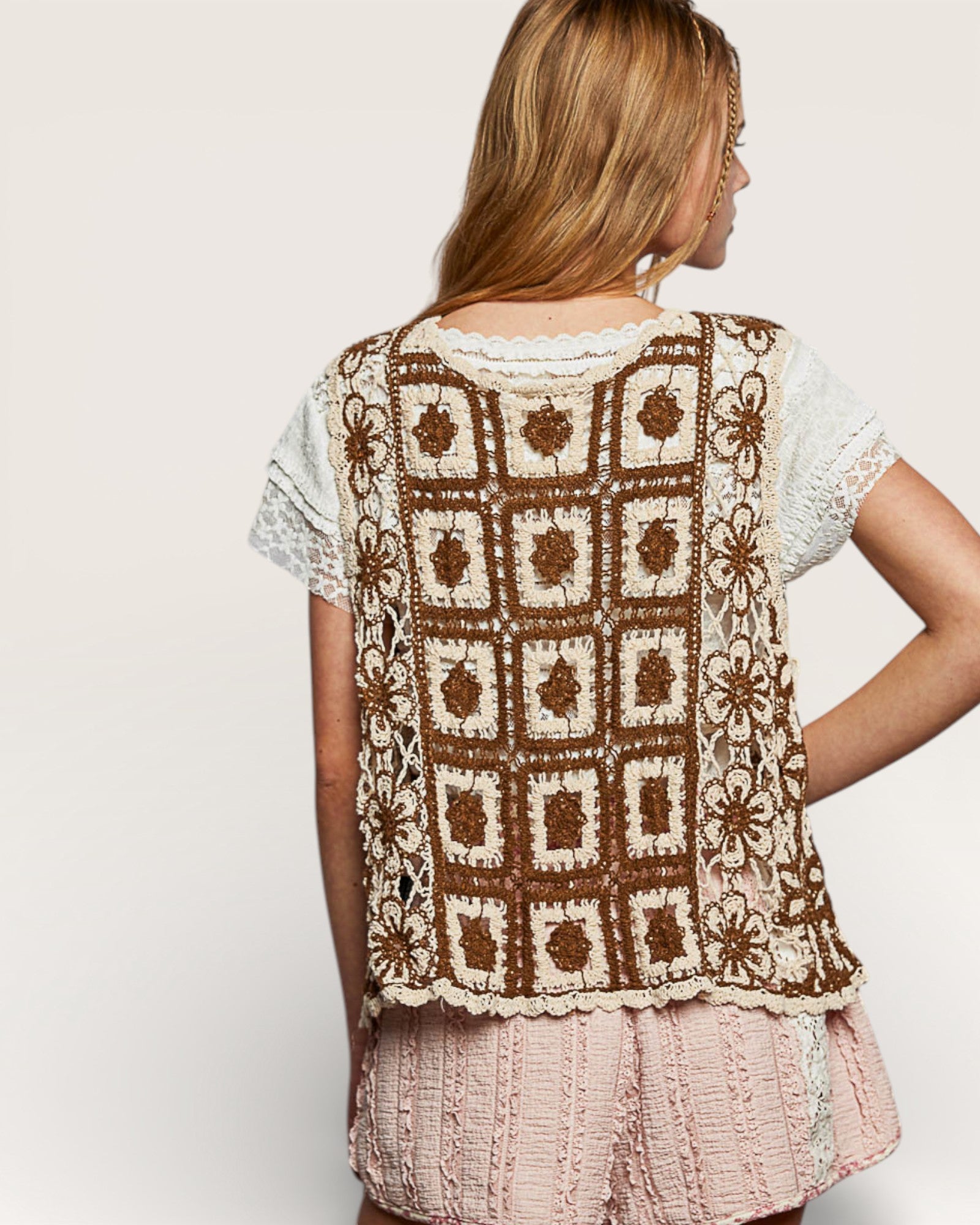 Woman wearing a brown and white crochet top with a plain background