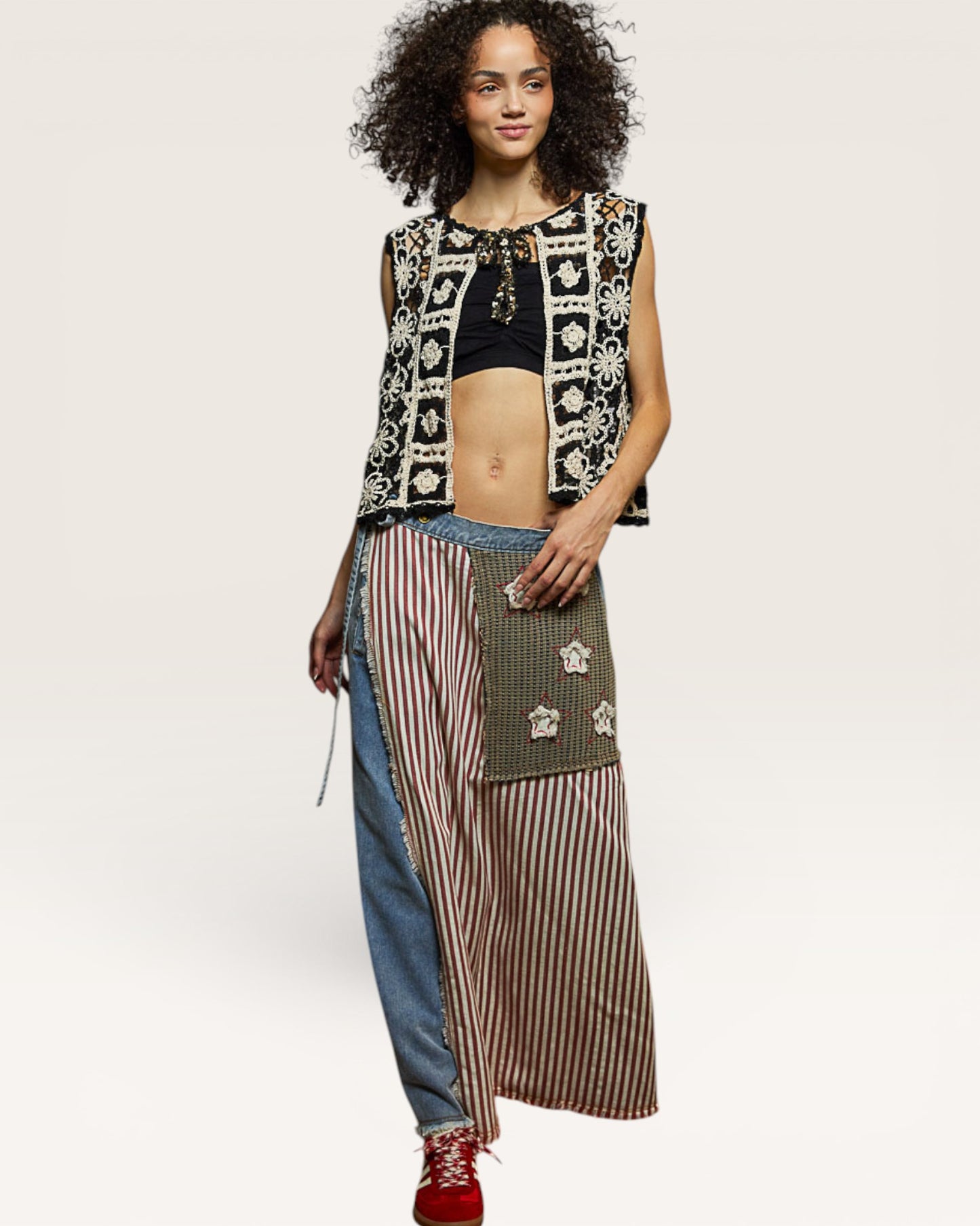 Woman wearing a patterned sleeveless top and long, multicolored skirt on a white background