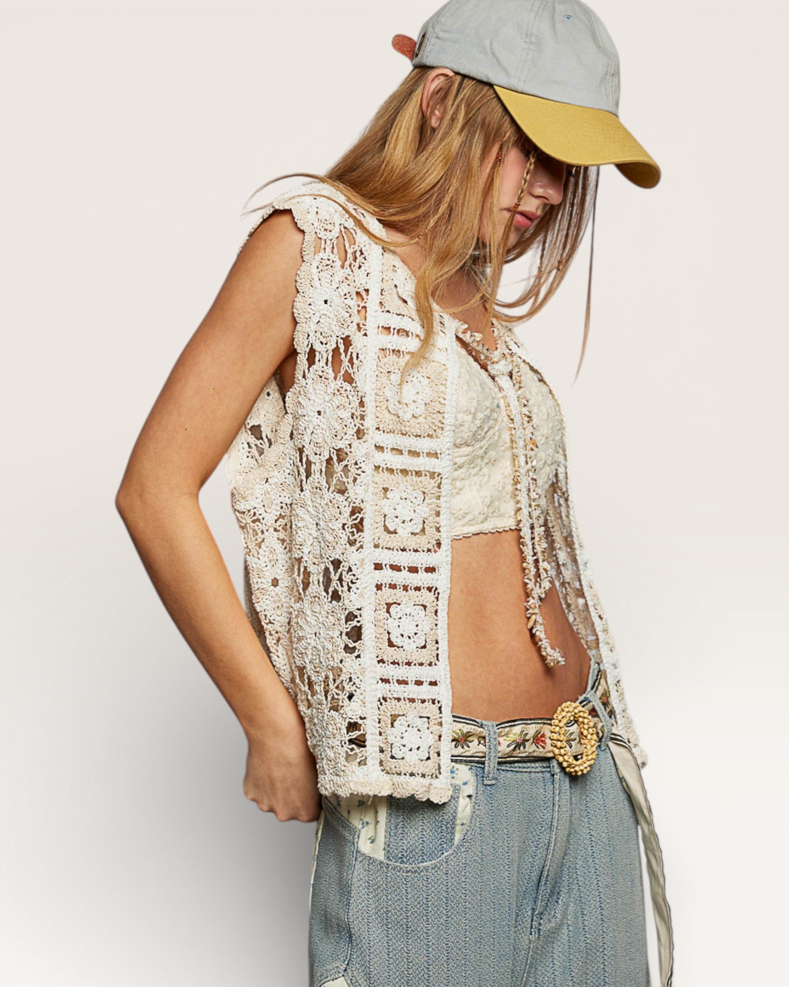 Person wearing a lace top, denim pants, and a cap on a plain background