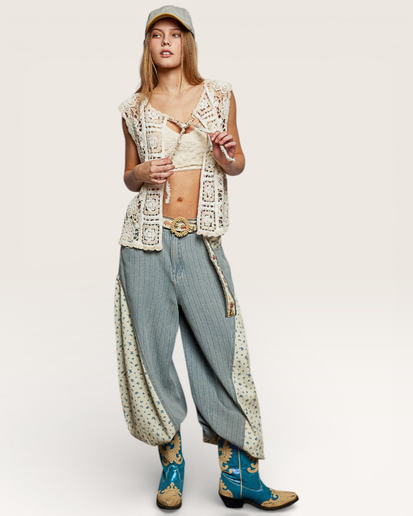 Person wearing a white lace top, blue jeans, and cowboy boots on a plain background