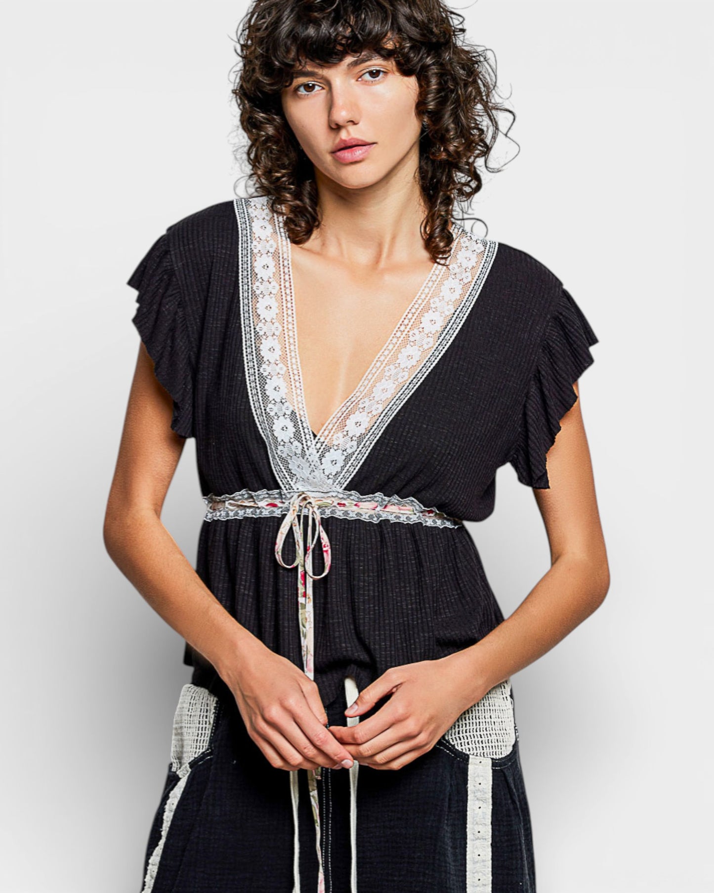 Woman wearing a black dress with white lace details on a light gray background