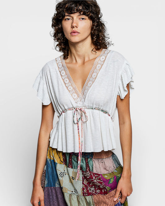 Woman wearing a white lace top with a colorful skirt on a plain background