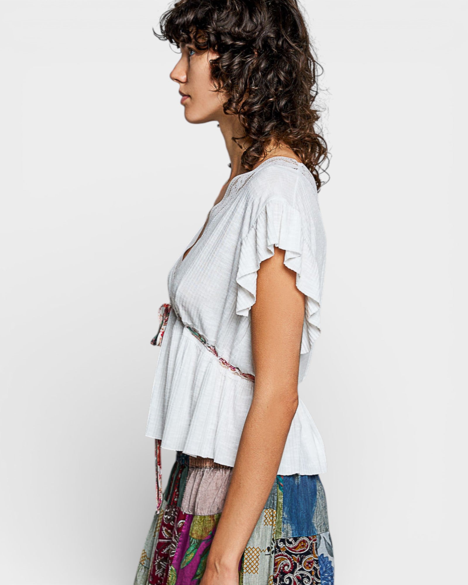Woman wearing a light gray top with ruffled sleeves on a plain background