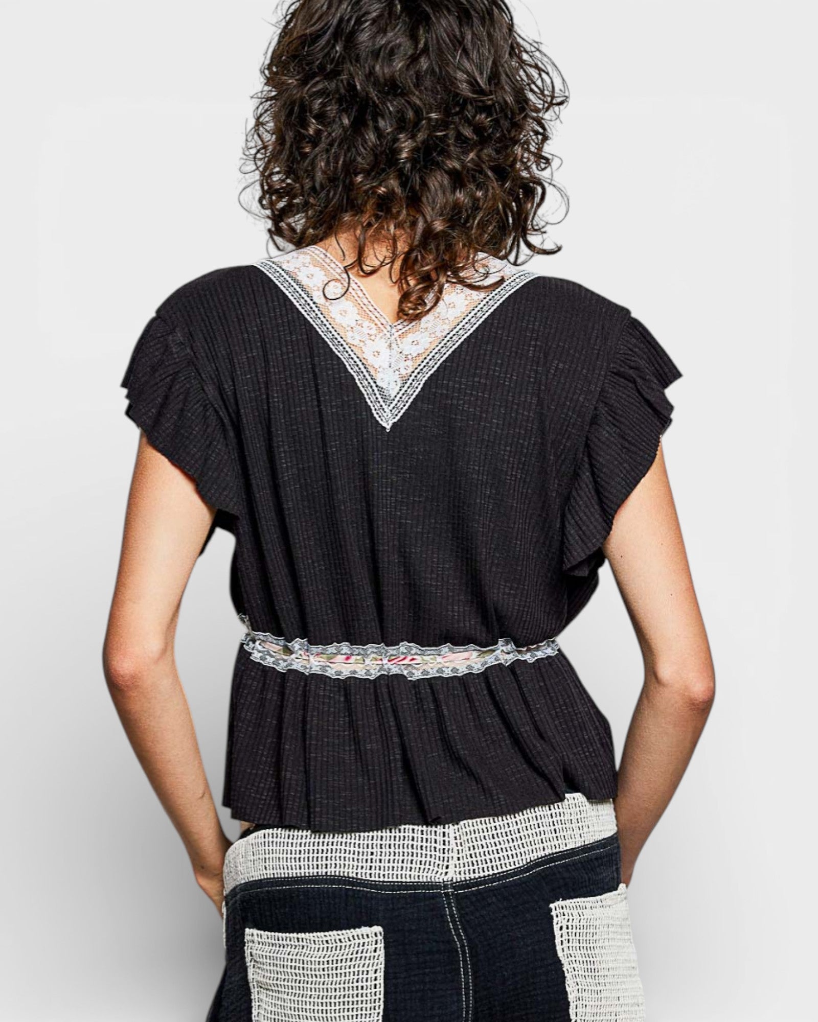 Person wearing a black top with lace details on a plain background