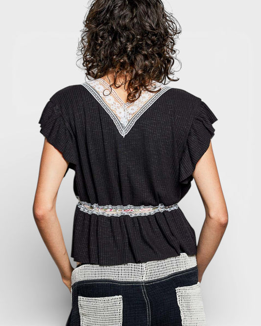 Person wearing a black top with lace details on a plain background