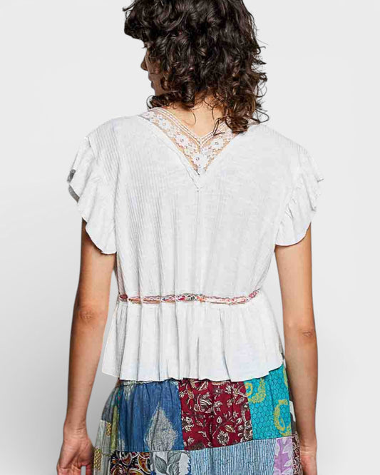 Woman wearing a white blouse with lace details and a colorful patterned skirt on a plain background