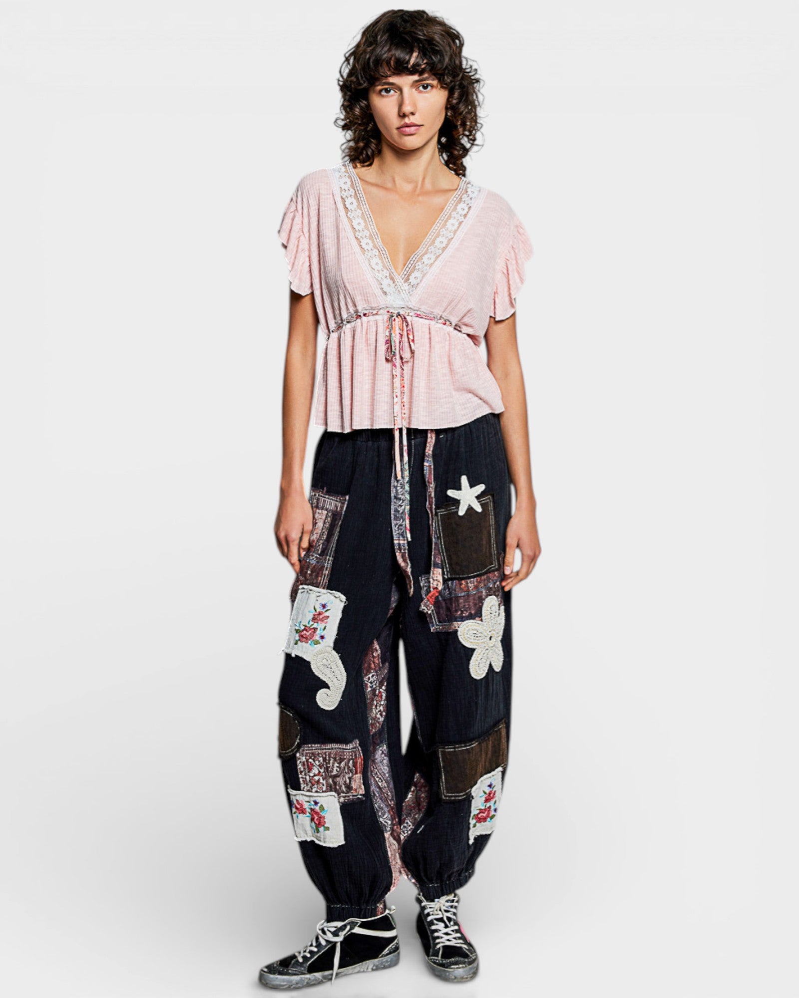 Woman wearing a pink top and patchwork pants on a white background