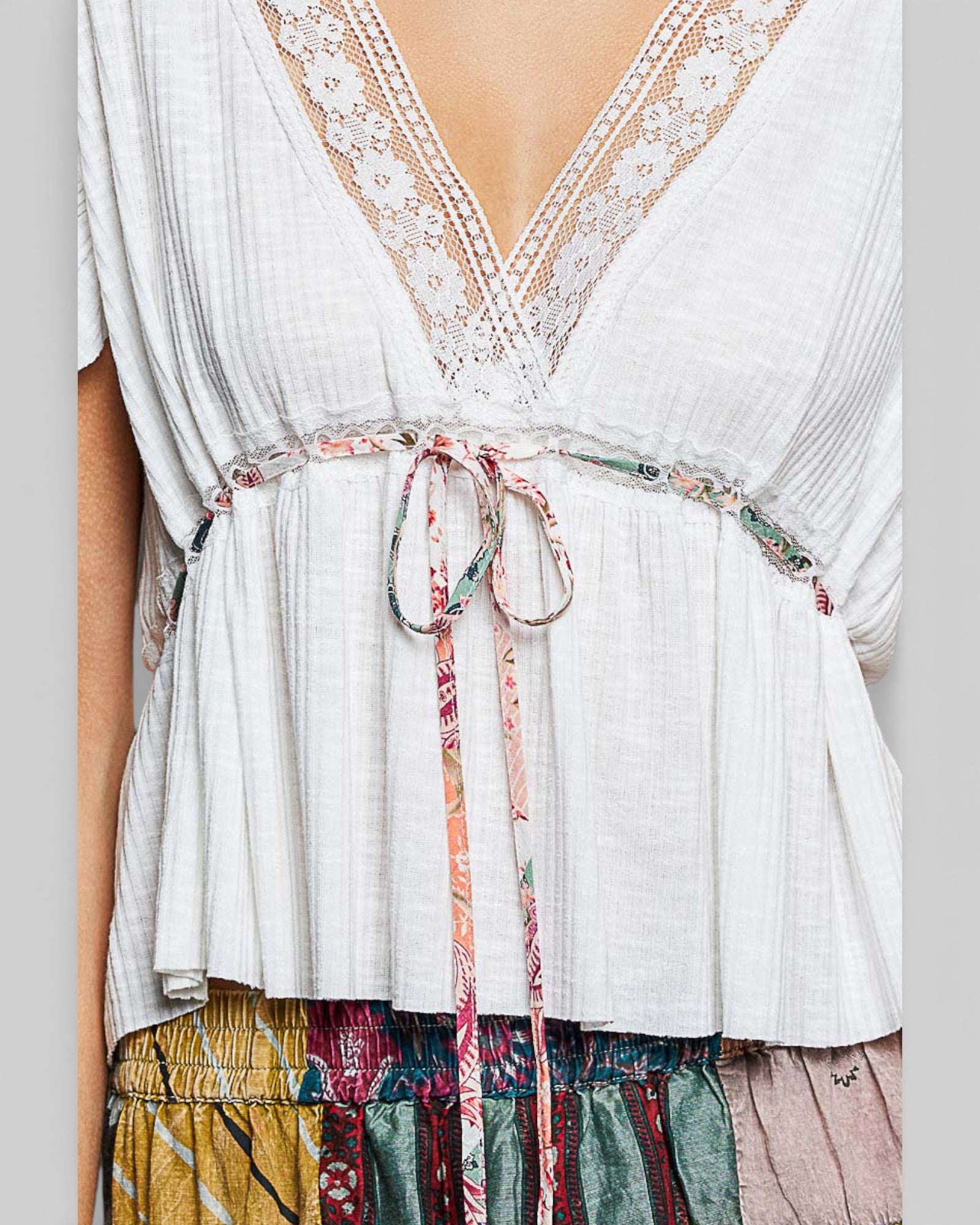 White lace-trimmed top with colorful tie and patterned bottom on a plain background