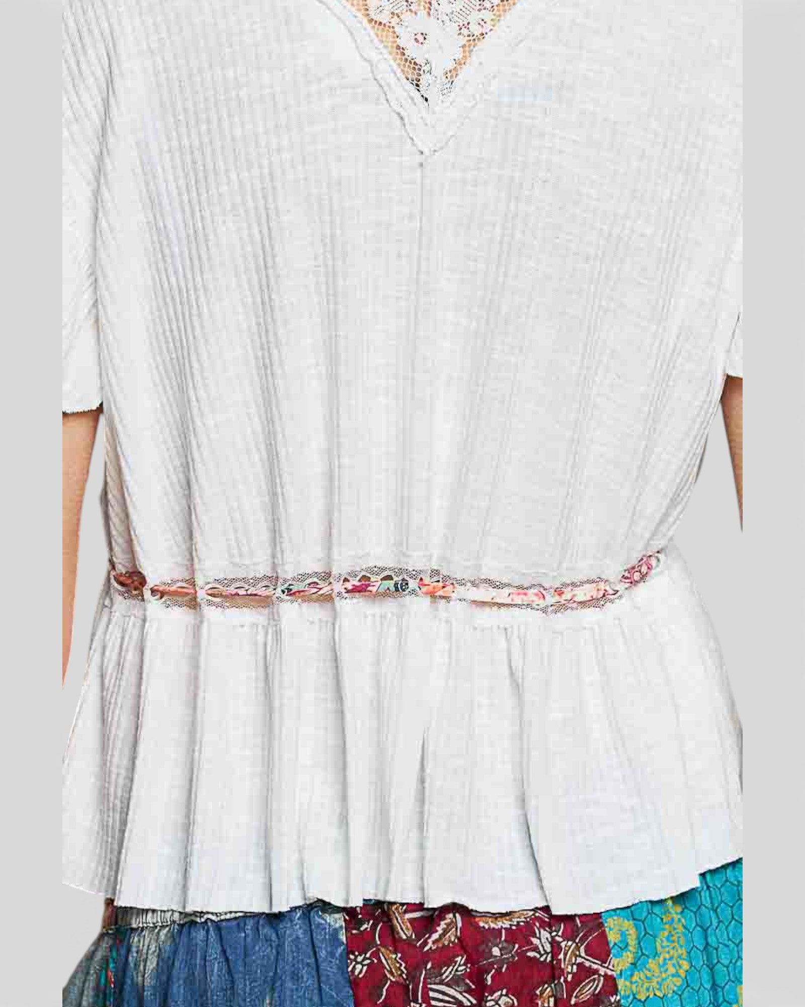 White blouse with a colorful belt and patterned skirt on a plain background
